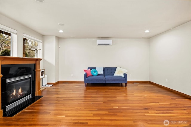 living area featuring baseboards, light wood-style flooring, a tiled fireplace, and a wall mounted AC