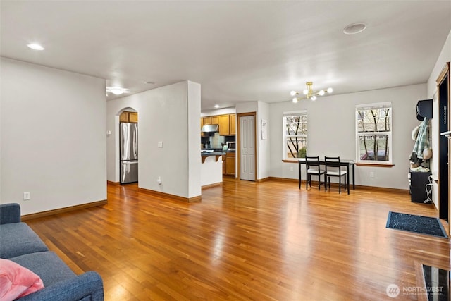 living room with baseboards, light wood-type flooring, recessed lighting, an inviting chandelier, and arched walkways