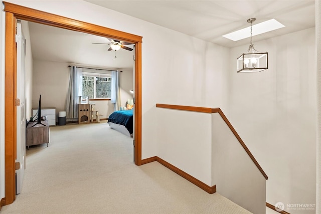 hall featuring baseboards, an upstairs landing, a skylight, and carpet flooring