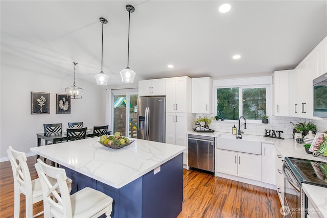 kitchen with hanging light fixtures, stainless steel appliances, a center island, sink, and white cabinets