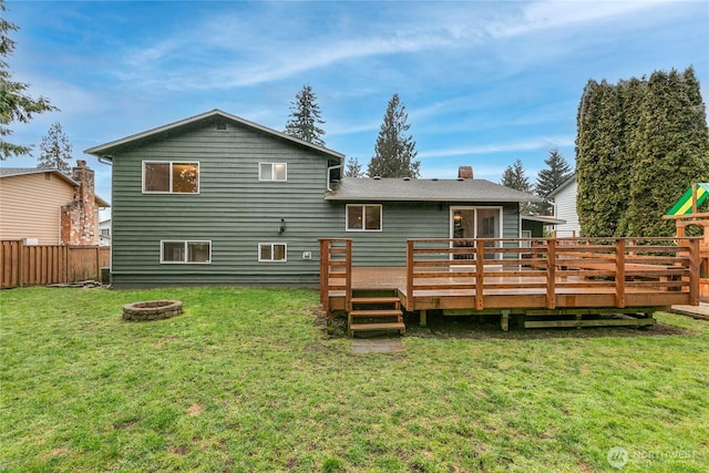 back of property with a yard, a wooden deck, and an outdoor fire pit