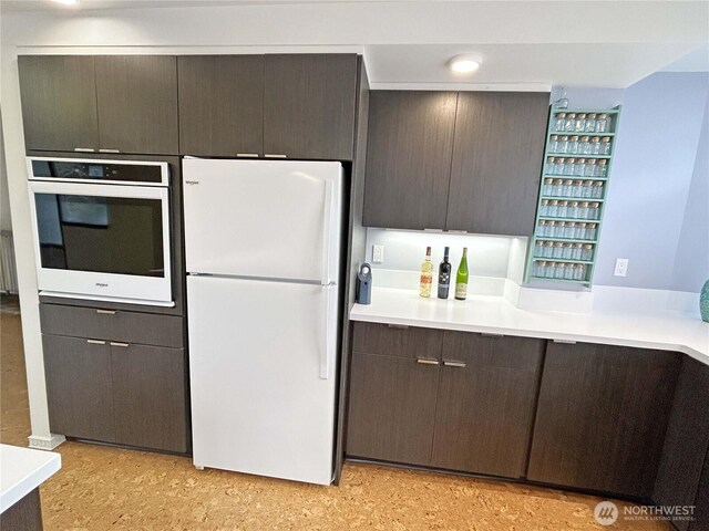 kitchen featuring white appliances, modern cabinets, light countertops, dark brown cabinets, and light floors