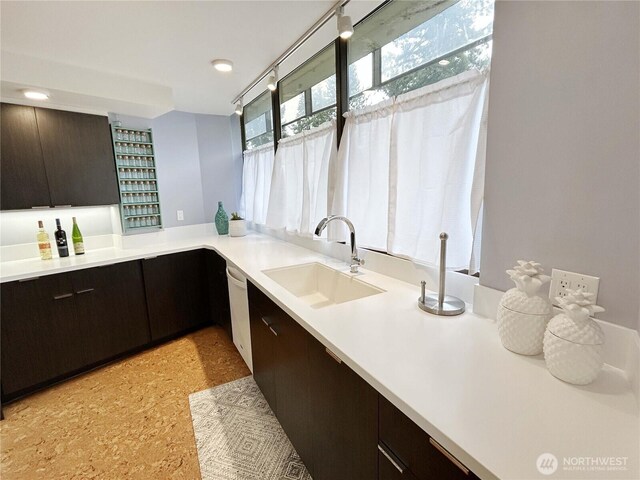 kitchen featuring dishwasher, light countertops, dark brown cabinets, and a sink