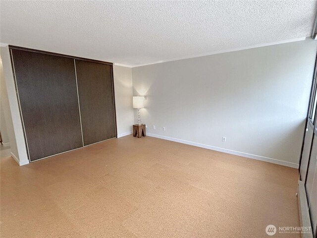 unfurnished bedroom featuring a textured ceiling, ornamental molding, a closet, and baseboards