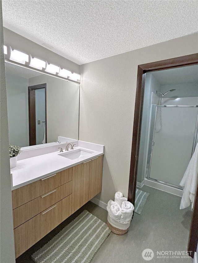 bathroom featuring a textured ceiling, a textured wall, vanity, baseboards, and a shower stall