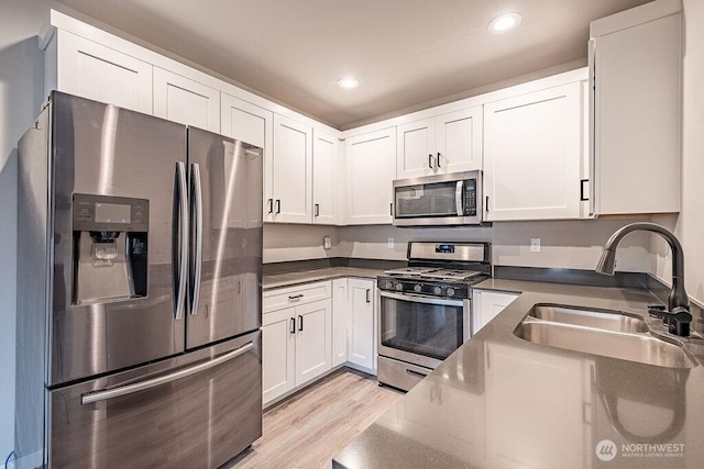 kitchen with stainless steel appliances, dark countertops, a sink, and white cabinets