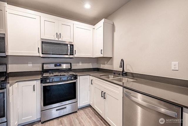 kitchen featuring white cabinets, dark countertops, appliances with stainless steel finishes, light wood-style floors, and a sink