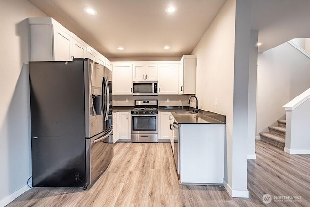 kitchen featuring white cabinets, dark countertops, light wood-style flooring, appliances with stainless steel finishes, and a sink