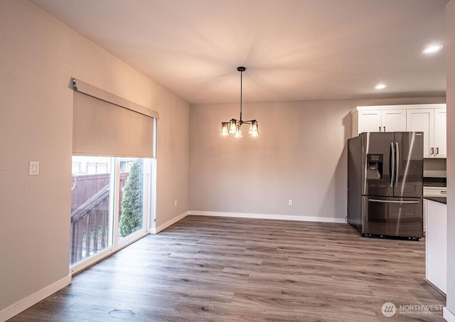 unfurnished dining area with a notable chandelier, recessed lighting, wood finished floors, and baseboards