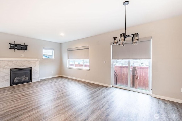 unfurnished living room with an inviting chandelier, a fireplace, baseboards, and wood finished floors