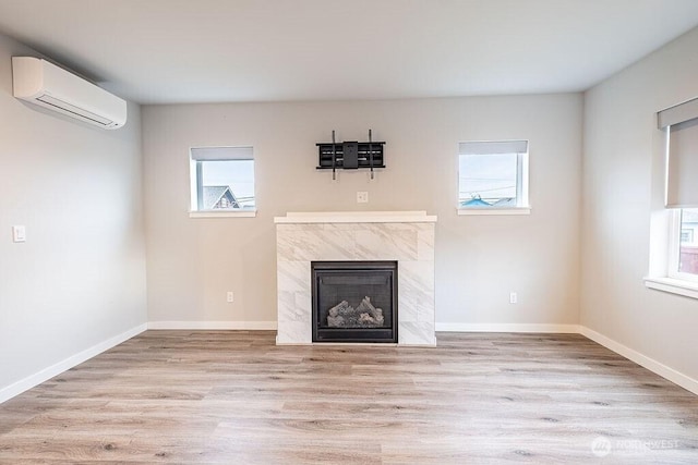 unfurnished living room featuring a high end fireplace, a wealth of natural light, light wood-type flooring, and a wall mounted air conditioner