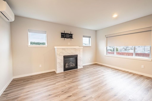 unfurnished living room with light wood finished floors, a premium fireplace, baseboards, and an AC wall unit