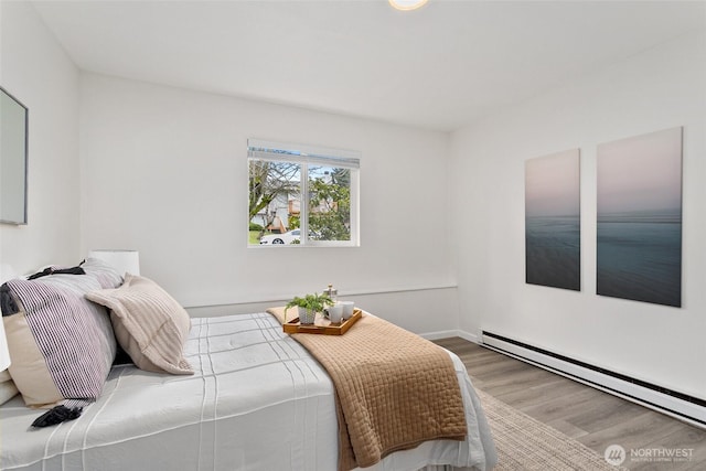 bedroom featuring a baseboard heating unit, wood finished floors, and baseboards