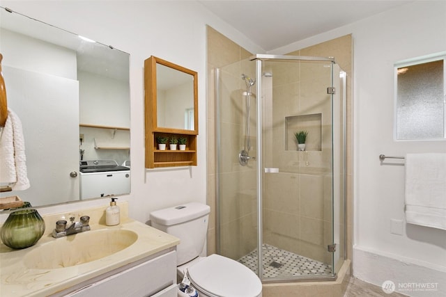 bathroom featuring washing machine and dryer, a shower stall, vanity, and toilet