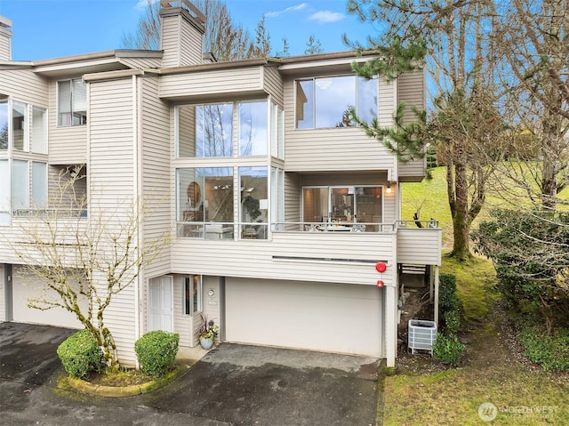 view of front of home with a garage, central AC unit, a balcony, a chimney, and aphalt driveway