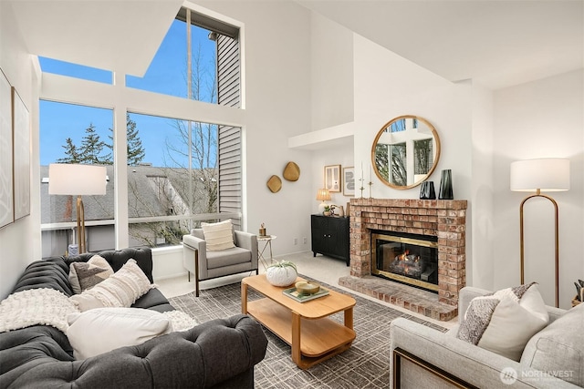 living area with a towering ceiling, a brick fireplace, carpet, and baseboards