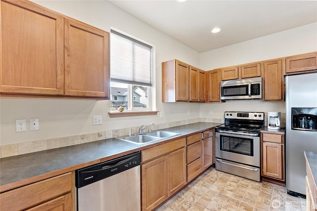 kitchen featuring dark countertops, stainless steel appliances, recessed lighting, a sink, and brown cabinetry