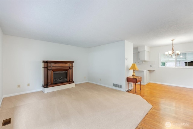 living room featuring visible vents, baseboards, an inviting chandelier, and a fireplace with raised hearth