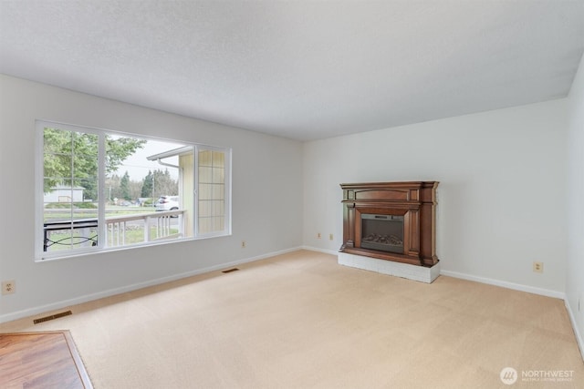 unfurnished living room featuring light carpet, visible vents, a fireplace with raised hearth, and baseboards