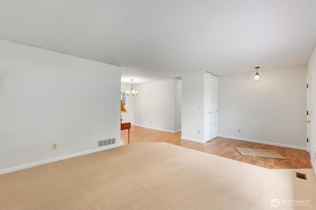 empty room with a notable chandelier, baseboards, visible vents, and a textured ceiling