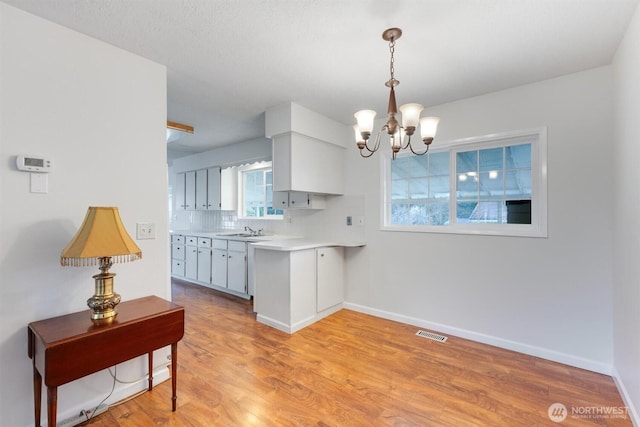 kitchen featuring visible vents, a sink, backsplash, light wood-style floors, and an inviting chandelier