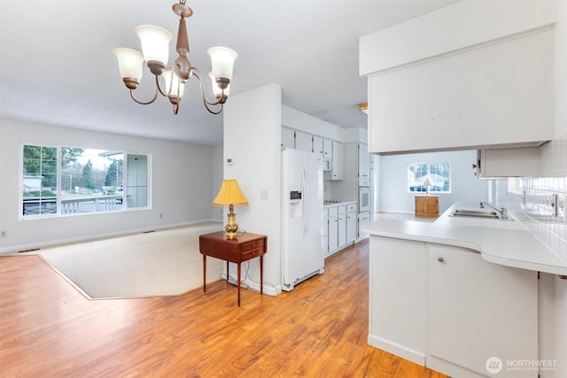 kitchen featuring light wood-type flooring, a sink, white appliances, an inviting chandelier, and light countertops