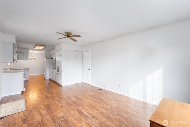 unfurnished living room with light wood-style flooring, ceiling fan with notable chandelier, baseboards, and a sink