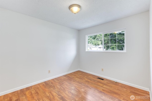 empty room featuring visible vents, baseboards, a textured ceiling, and light wood-style flooring