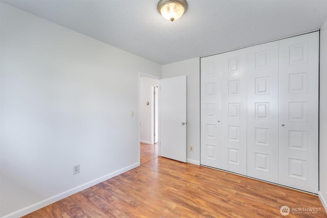 unfurnished bedroom featuring light wood finished floors, a textured ceiling, a closet, and baseboards