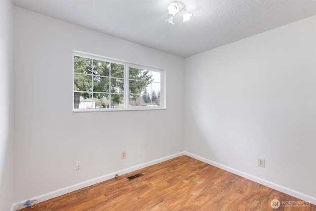 spare room featuring visible vents, a textured ceiling, baseboards, and wood finished floors