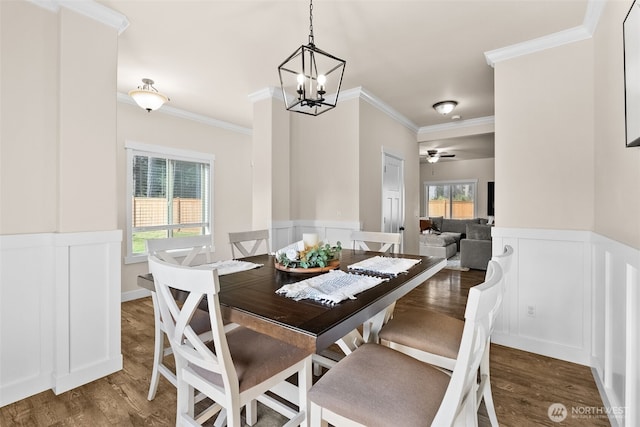 dining room with ceiling fan with notable chandelier, wainscoting, crown molding, and wood finished floors