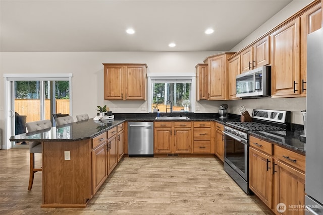 kitchen with a breakfast bar area, stainless steel appliances, a peninsula, a sink, and light wood-style floors