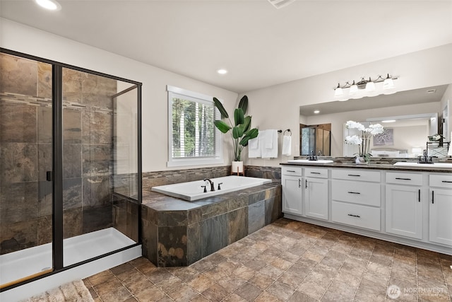 bathroom with double vanity, a bath, a shower stall, a sink, and recessed lighting