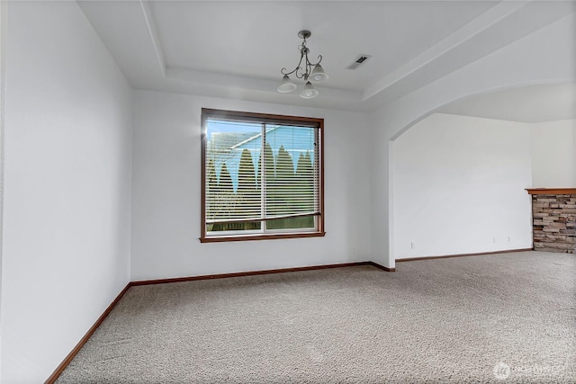 unfurnished room with baseboards, visible vents, arched walkways, a tray ceiling, and carpet flooring