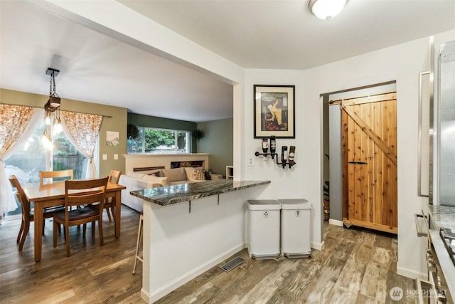 kitchen featuring a breakfast bar, pendant lighting, dark wood finished floors, a barn door, and a peninsula