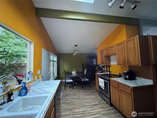 kitchen with stainless steel appliances, light countertops, lofted ceiling with beams, brown cabinetry, and a sink