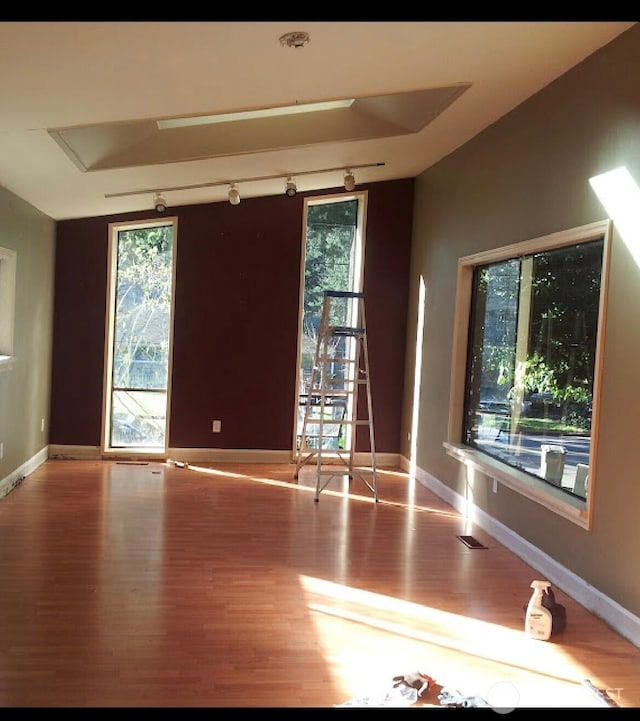 empty room with track lighting, light wood-type flooring, visible vents, and baseboards