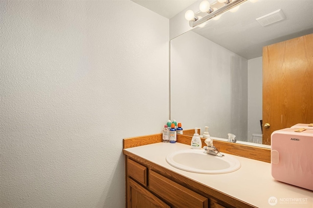 bathroom with a textured wall, vanity, and visible vents