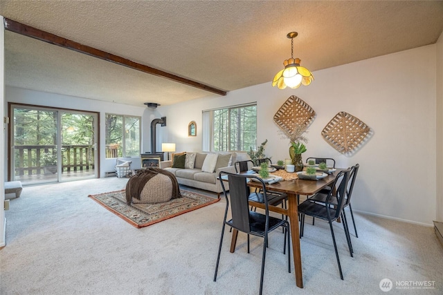 dining room with beamed ceiling, plenty of natural light, a wood stove, and light colored carpet