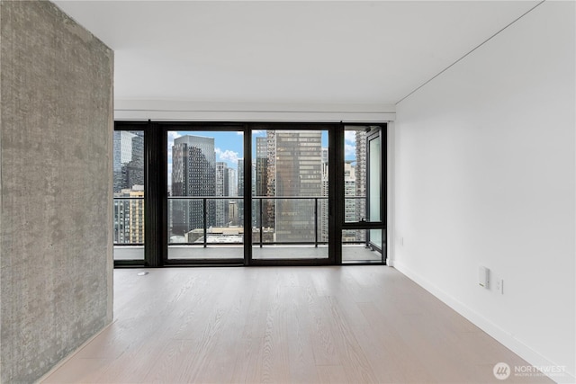 empty room featuring light wood-type flooring, a view of city, and baseboards