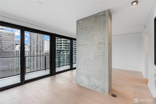 unfurnished room with light wood-type flooring, a city view, and baseboards