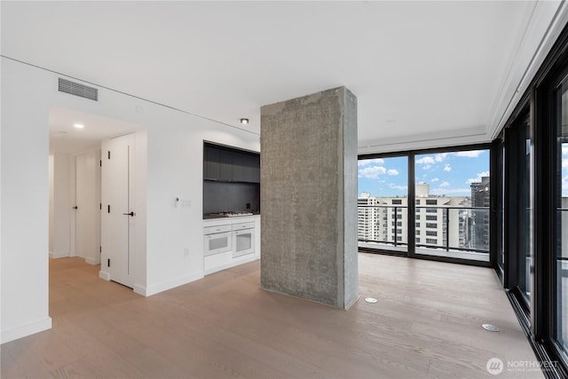 empty room with a view of city, light wood-style flooring, visible vents, baseboards, and expansive windows