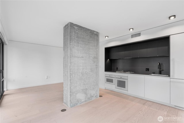 kitchen featuring modern cabinets, white oven, light countertops, white cabinetry, and a sink