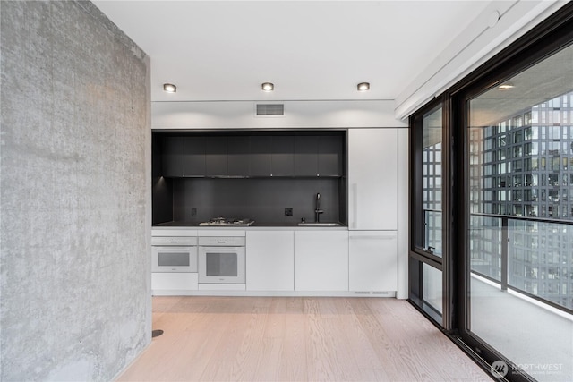 bar featuring light wood finished floors, visible vents, a sink, and white oven