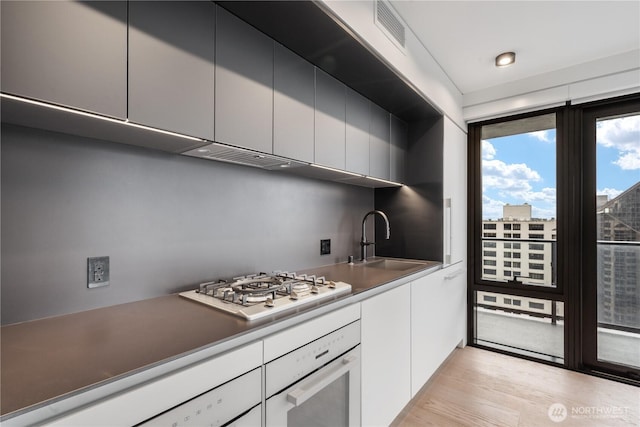 kitchen featuring a city view, a sink, white cabinetry, visible vents, and white oven