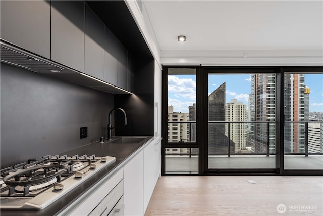 kitchen with a view of city, dark countertops, white cabinets, a sink, and gas cooktop