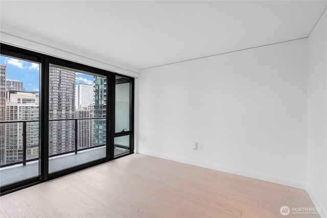 spare room featuring a view of city, light wood finished floors, and baseboards