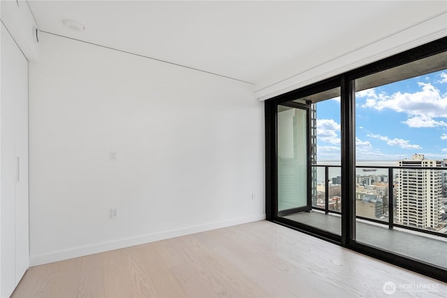 spare room featuring light wood-type flooring, a city view, and baseboards