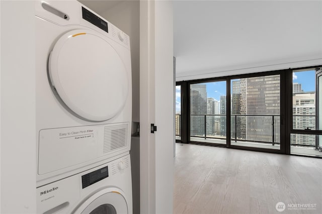 clothes washing area featuring a healthy amount of sunlight, light wood finished floors, a view of city, and stacked washer / drying machine