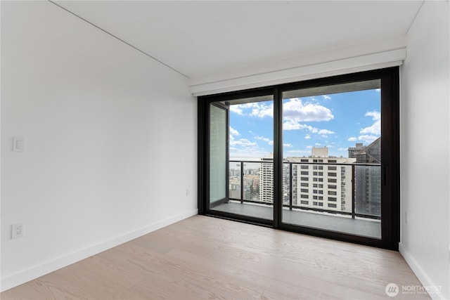 unfurnished room with a view of city, baseboards, and light wood-style floors